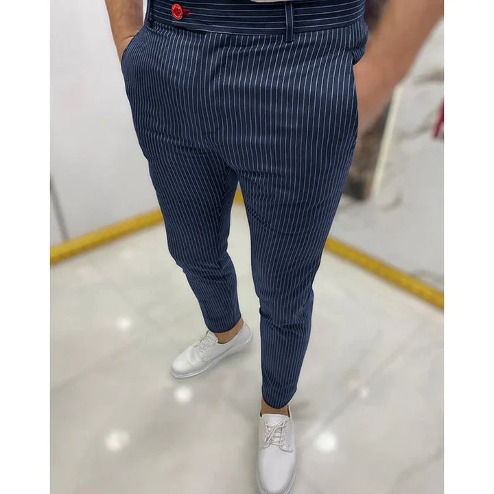 Man wearing navy blue pinstripe tapered pants with red button and white casual shoes on white floor
