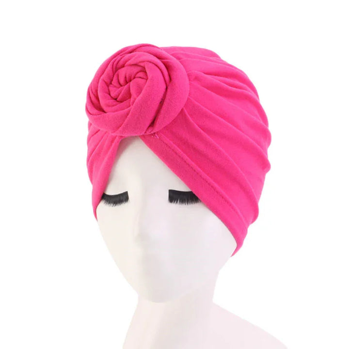 Bright pink turban headwrap with rose detail on white mannequin head with closed eyes