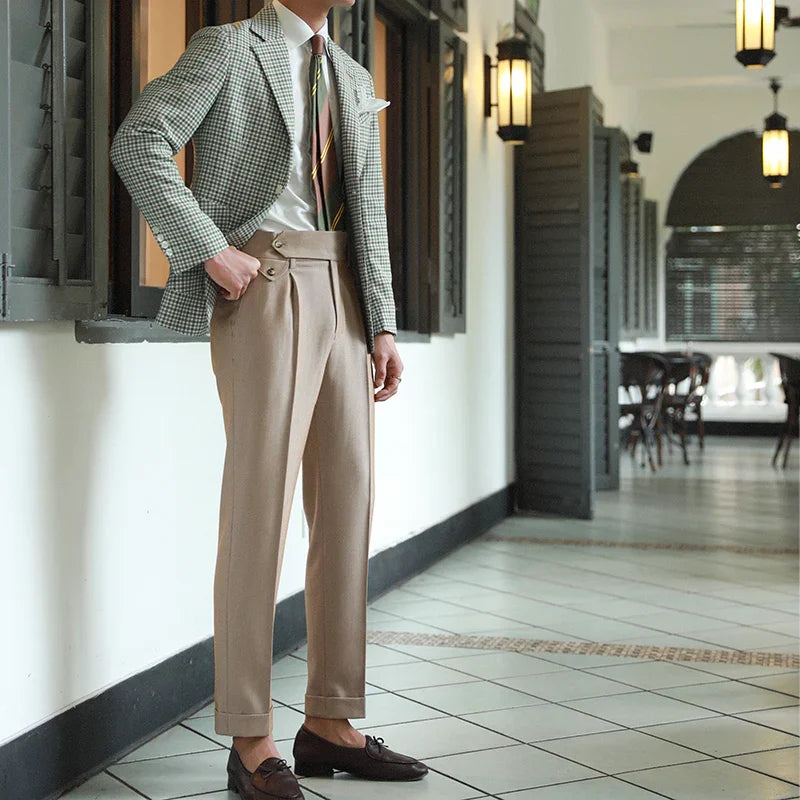 Man wearing high-waisted beige trousers, checkered blazer, striped tie, and black loafers in hallway