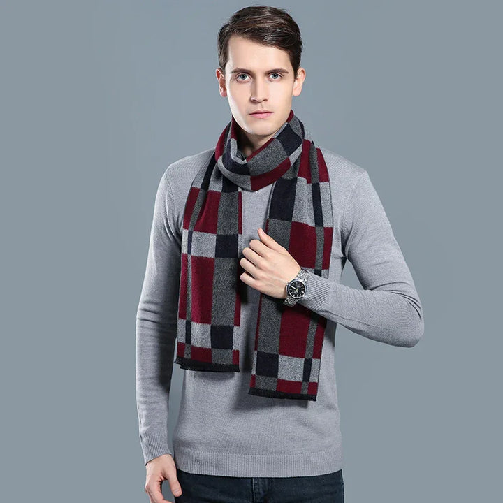 Man wearing a gray sweater and plaid scarf in red, black, and gray against gray background