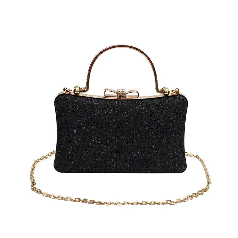 Black glitter evening clutch handbag with gold bow clasp, top handle, and gold chain strap