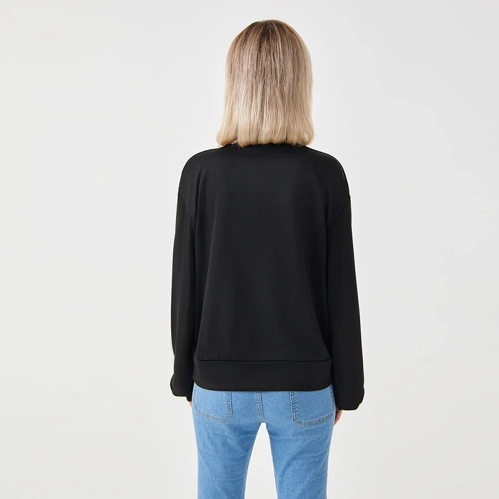 Woman wearing black long-sleeve sweatshirt and light blue jeans facing away on white background