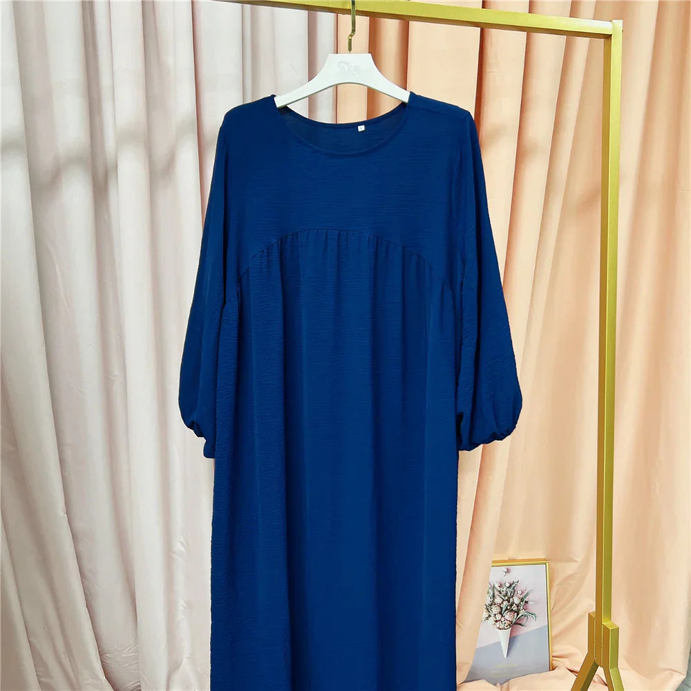 blue long-sleeve loose dress on white hanger against beige curtains and framed floral art