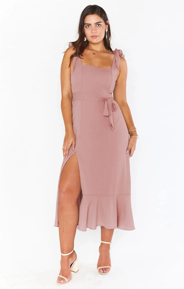 Woman wearing mauve sleeveless midi dress with side slit and tie shoulder straps, white heels