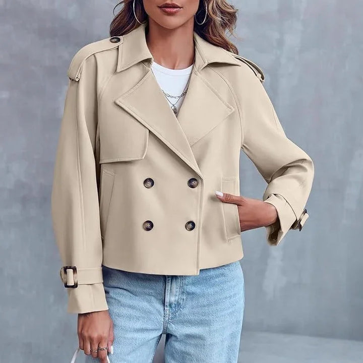 Woman wearing beige cropped double-breasted trench coat with button details and light blue jeans