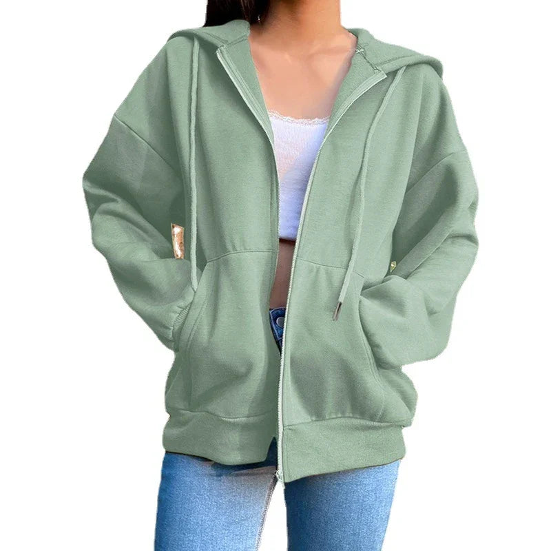 Woman wearing oversized sage green zip-up hoodie with front pockets and drawstring hood
