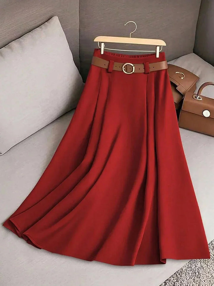 Red pleated midi skirt with brown belt on wooden hanger on gray couch with brown handbags