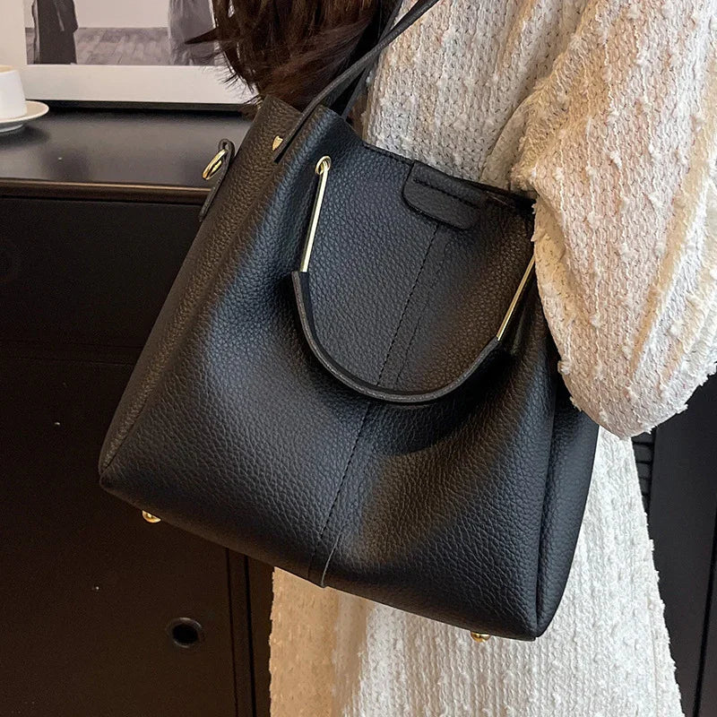 Black leather tote handbag with gold hardware worn on shoulder by person in textured cream sweater