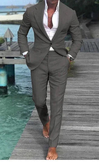 Man wearing gray suit with white shirt, walking barefoot on wooden dock by turquoise water