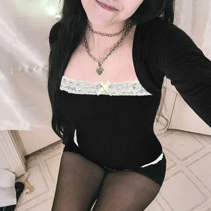 Woman wearing black lace-trimmed top with bow and chain necklace, sitting on tiled floor