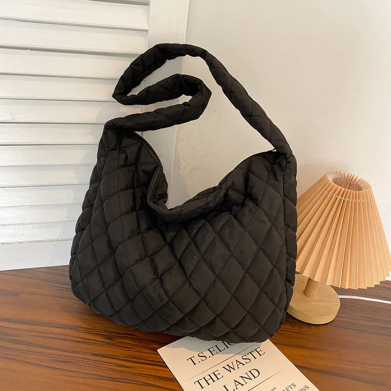 Black quilted shoulder bag on wooden table next to a pleated wooden lamp and a T.S. Eliot book
