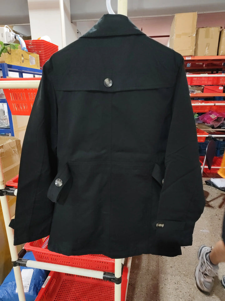 Black trench coat hanging on a white rack in a storage room with red plastic baskets and cardboard boxes