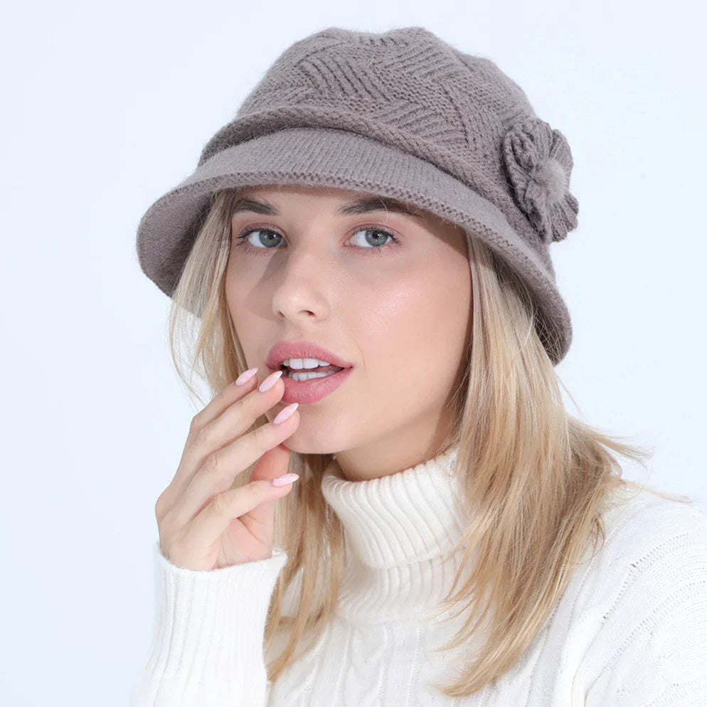 Woman wearing a taupe knitted wool hat with flower detail and white cable knit turtleneck sweater