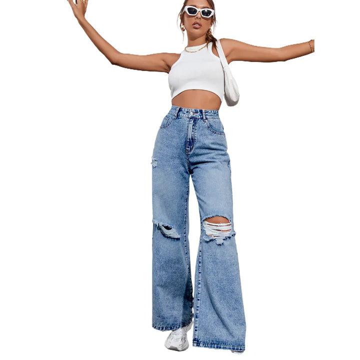 Woman wearing white crop top, ripped wide-leg jeans, white sneakers, sunglasses, and shoulder bag