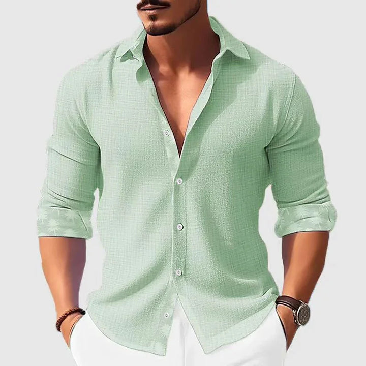 Man wearing casual light green button-up shirt with rolled sleeves and white pants