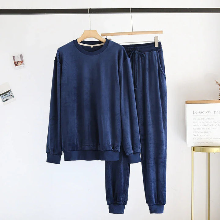 navy blue velour sweatshirt and jogger pants set hanging on wooden hangers against white wall