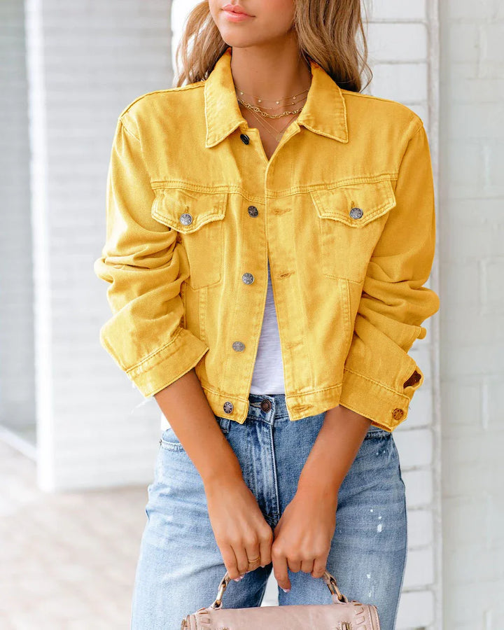 Woman wearing a yellow denim jacket with rolled sleeves and blue jeans holding a beige handbag