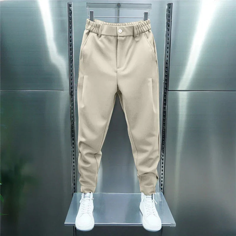 Beige tapered jogger pants with elastic waistband and white sneakers on display against metallic background