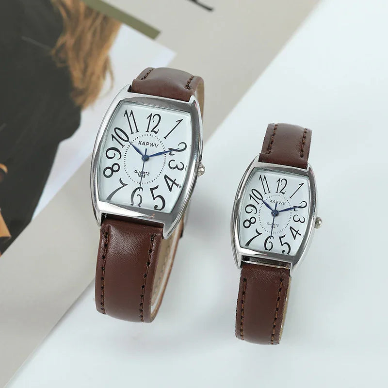 Two wristwatches with white distorted numeral dials and brown leather straps on a white surface