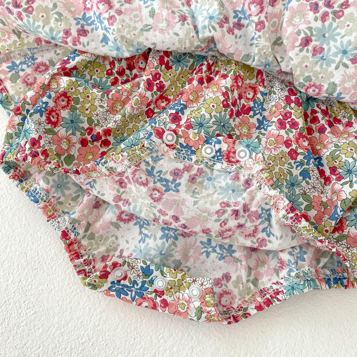 Baby floral romper with pink, red, blue, and green flowers and snap closures on white background