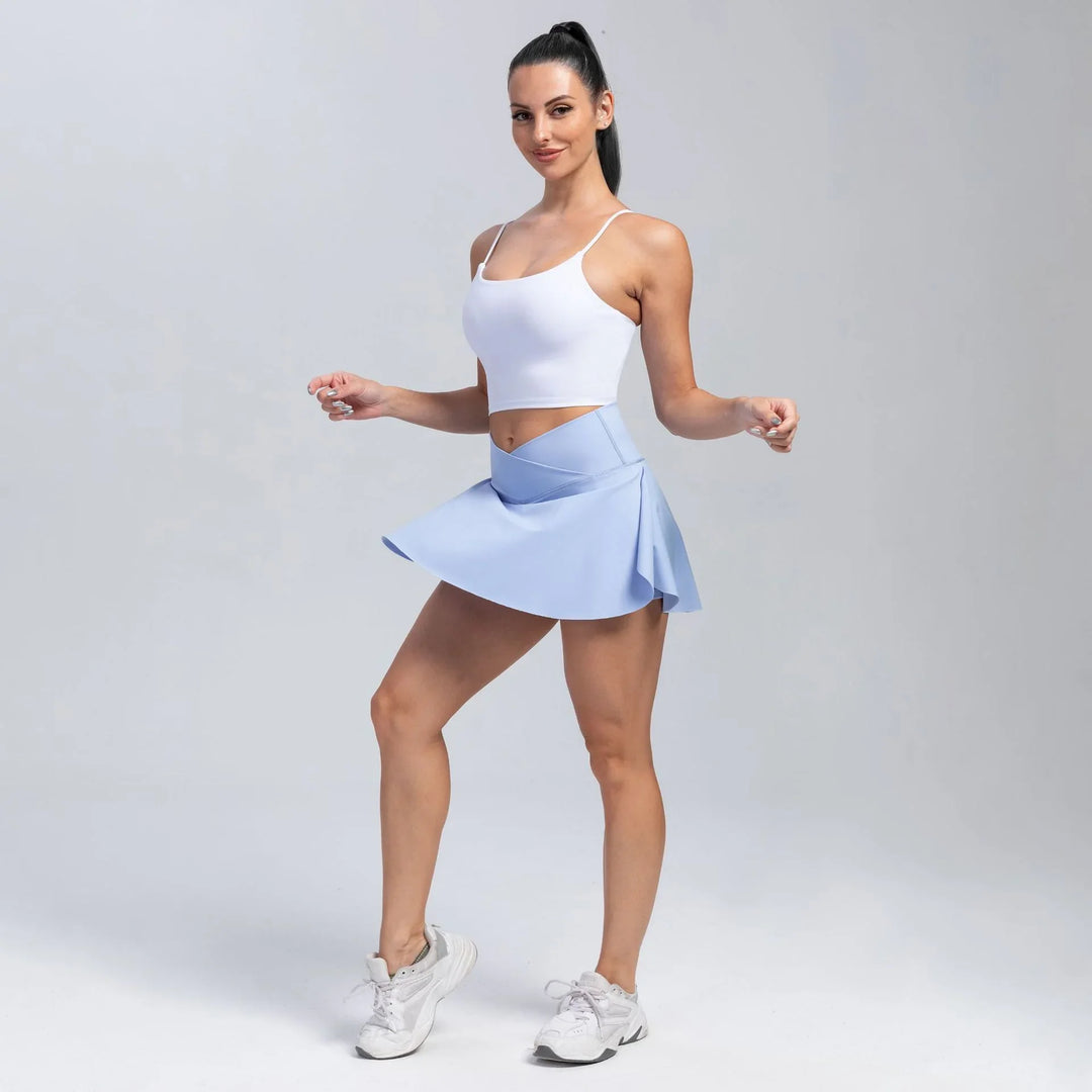 fit woman in white crop top and light blue athletic skort posing in studio with white sneakers