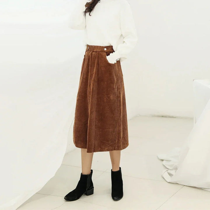 Woman wearing brown corduroy midi skirt with pockets and black ankle boots in minimalist white setting