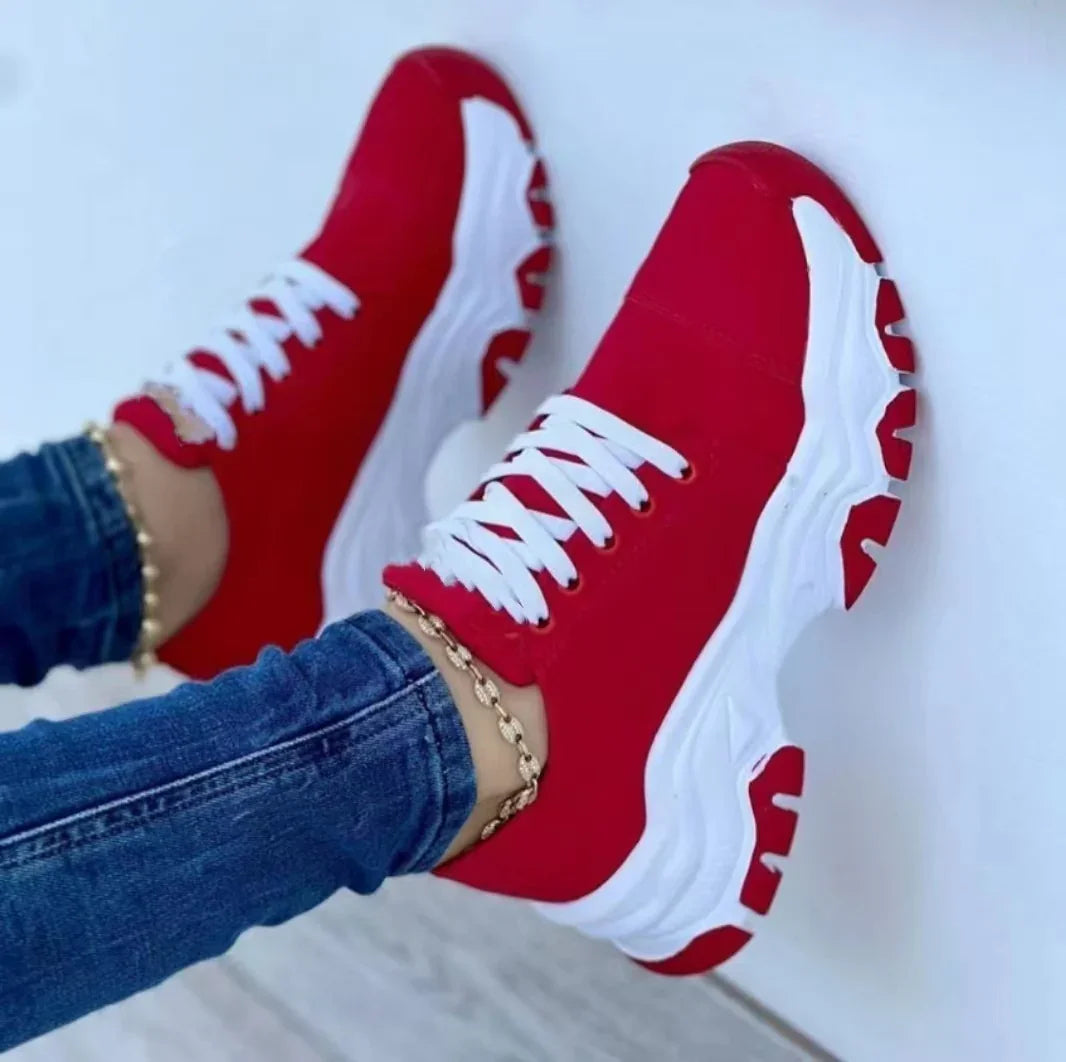 Red and white chunky sneakers with white laces worn with blue jeans and gold anklet on white background
