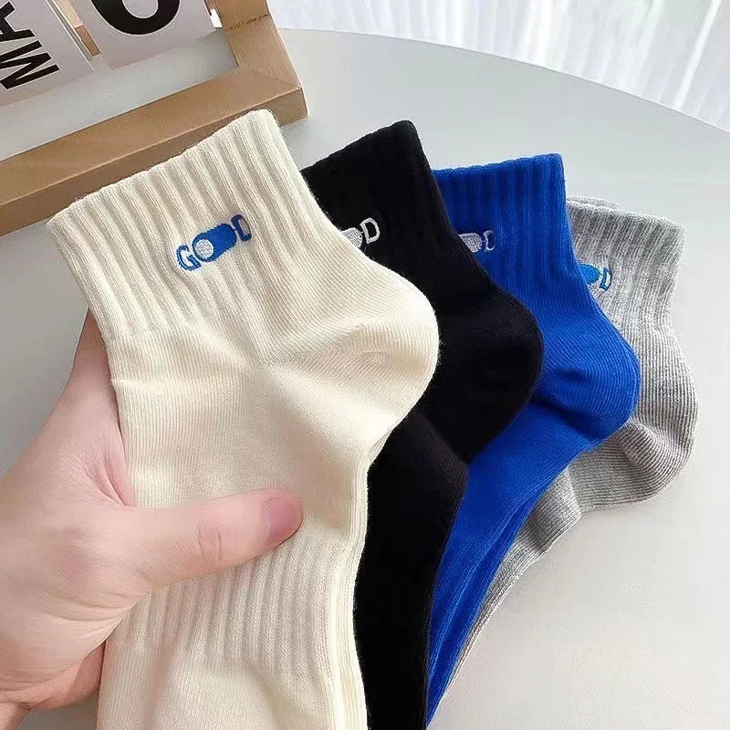 Hand holding beige ribbed socks with blue and white logo, next to black, blue, and gray socks