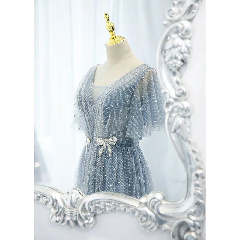 Elegant blue tulle dress with pearl details and bow belt displayed on mannequin in ornate silver mirror reflection