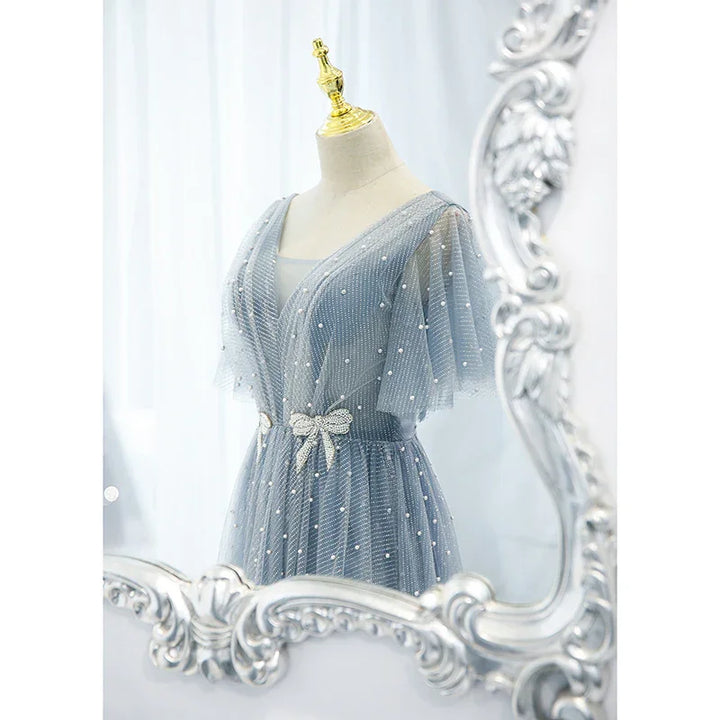 Elegant blue tulle dress with pearl details and bow belt displayed on mannequin in ornate silver mirror reflection