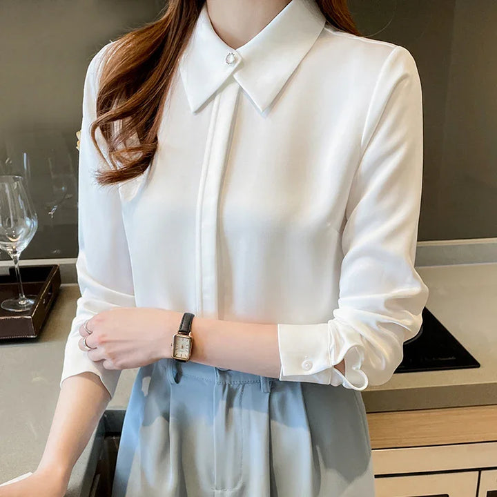 Woman wearing a white long-sleeve blouse with pearl collar button and light blue pants, standing in modern kitchen