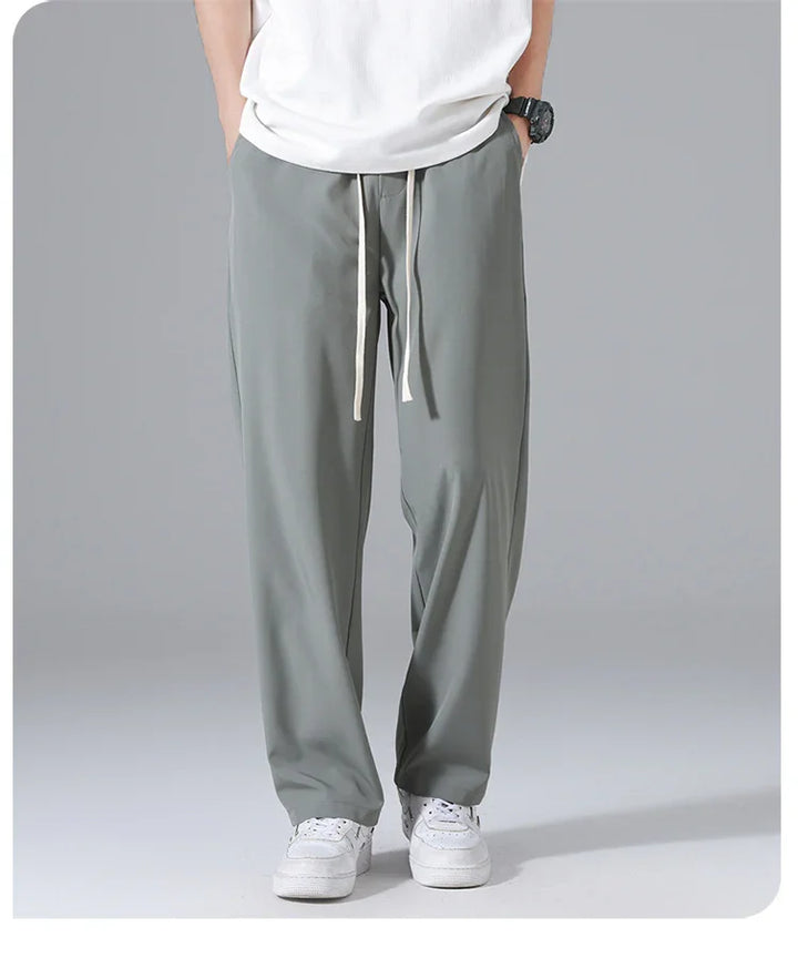 Person wearing grey drawstring pants and white sneakers against plain gray background