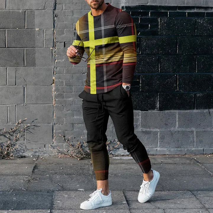 Man wearing trendy black and yellow plaid sweater with black joggers and white sneakers against gray brick wall