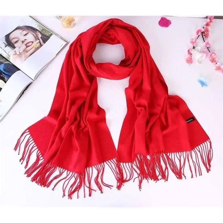 Bright red soft scarf with fringed edges laid out on white surface with flowers and open magazine
