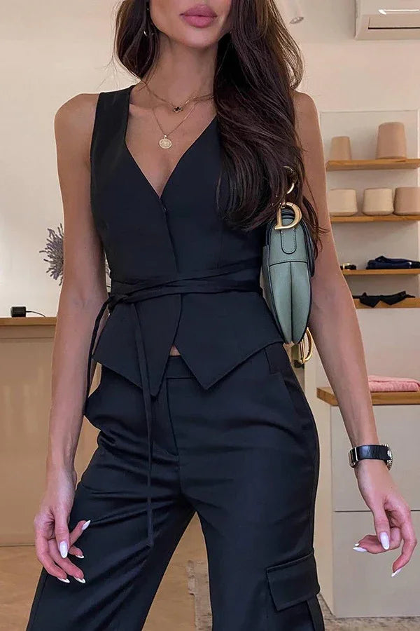 woman wearing sleeveless black wrap top and matching black pants with green handbag on shoulder indoors