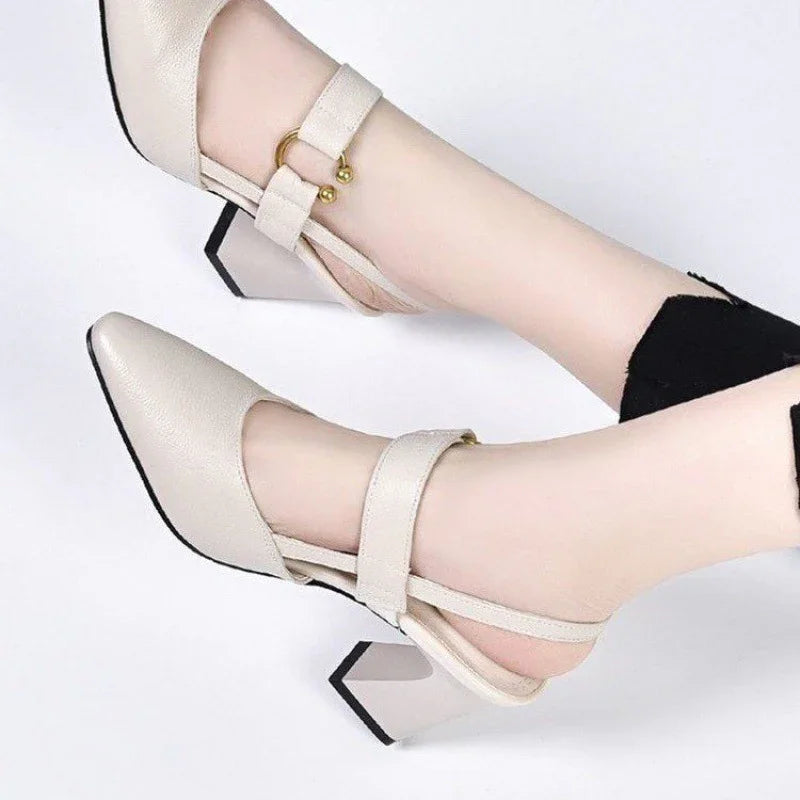 Beige leather block heel shoes with ankle straps and gold ball buckle details on feet against white background