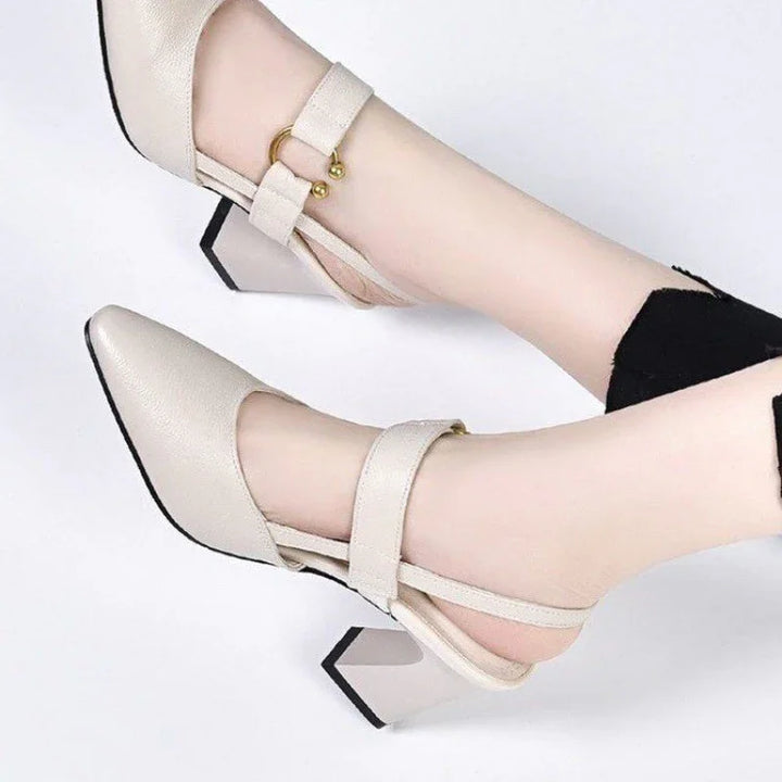 Beige leather block heel shoes with ankle straps and gold ball buckle details on feet against white background