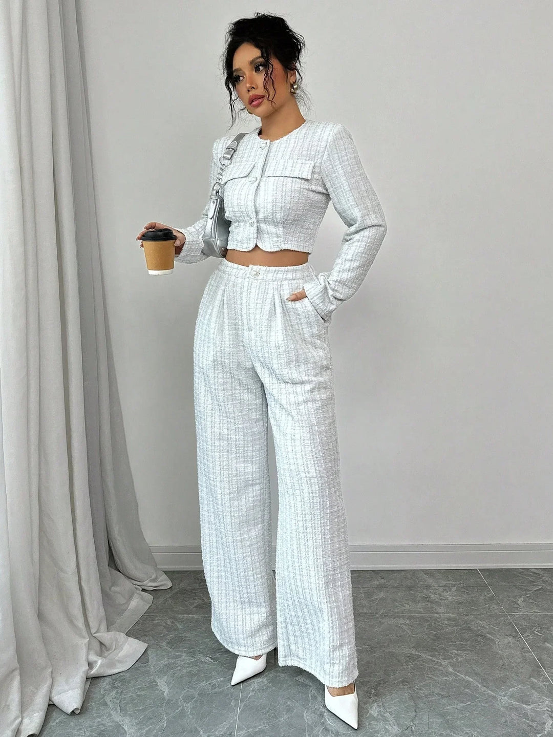 Woman wearing white textured two-piece outfit with cropped jacket and wide-leg pants, holding coffee cup