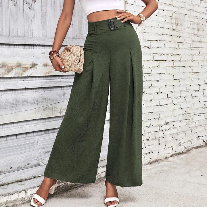 Woman wearing high-waist olive green wide-leg pants with belt and white crop top, standing against white brick wall
