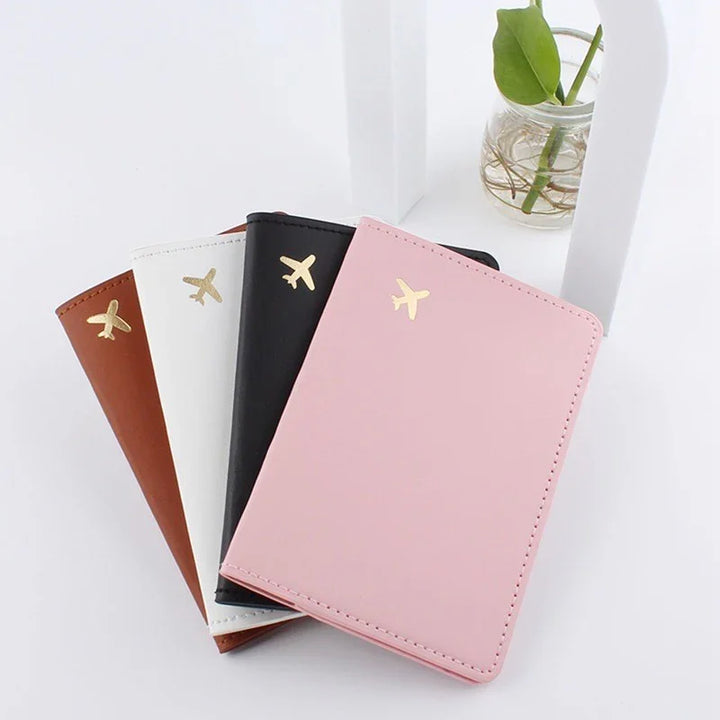 Set of four passport holders in pink, black, white, and brown with gold airplane icons on a white surface