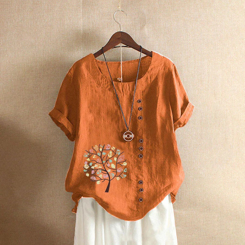 Orange short-sleeve linen blouse with buttons and tree print, paired with white pants on hanger
