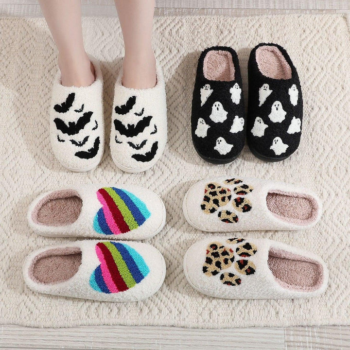 Collection of cozy fleece slippers with bat, ghost, rainbow heart, and leopard print patterns on a textured rug