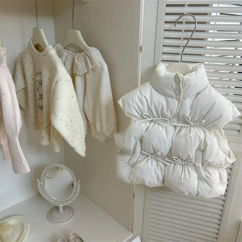 White padded sleeveless vest with drawstring hanging near cozy knit sweaters on white hangers