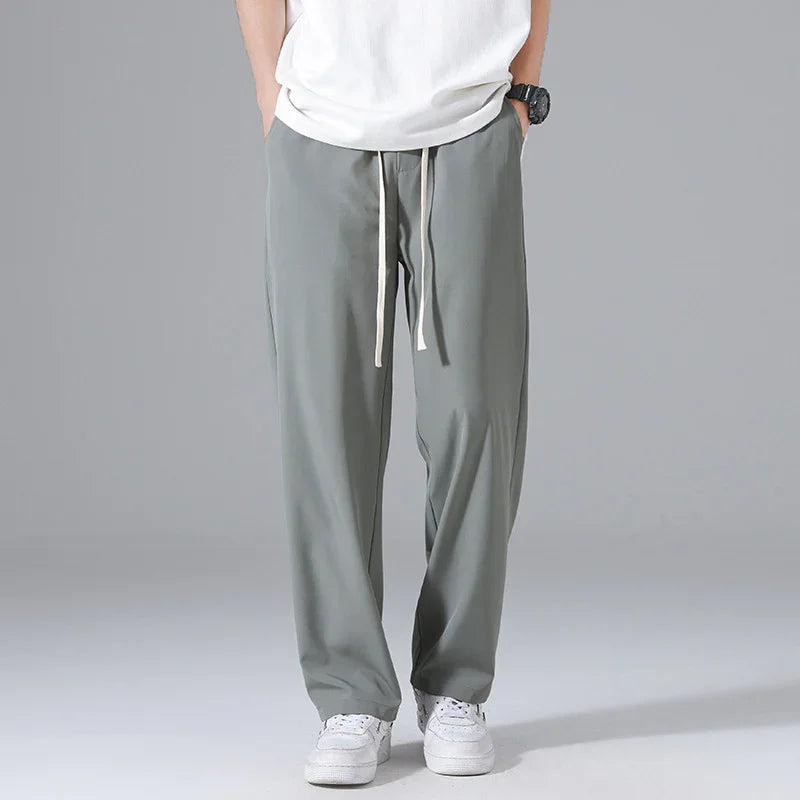 Man wearing gray casual drawstring pants with white sneakers and a white T-shirt on plain background