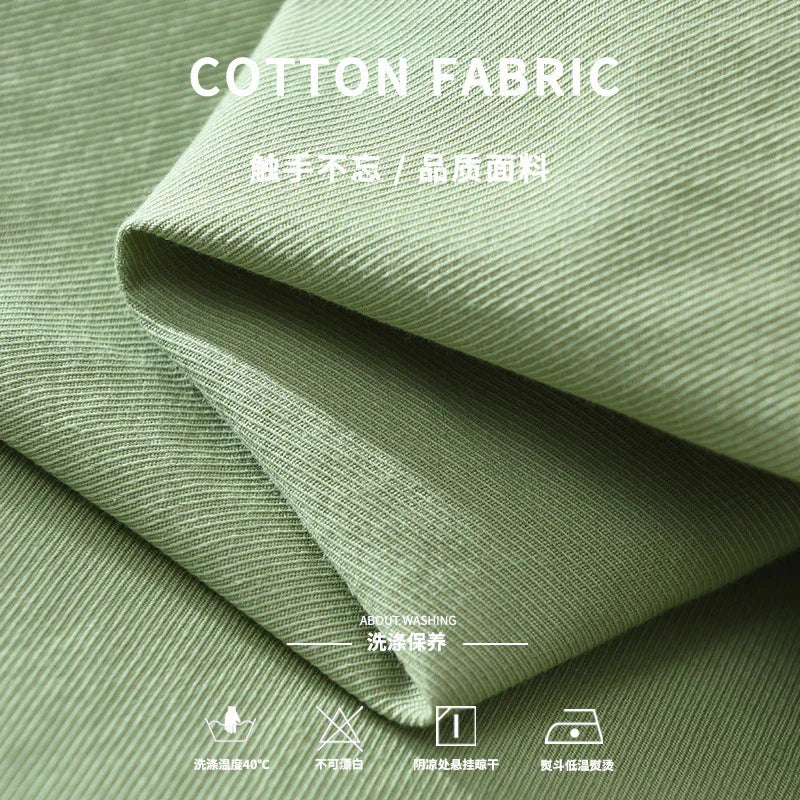 Close-up of soft green cotton fabric with visible weave texture and washing care symbols