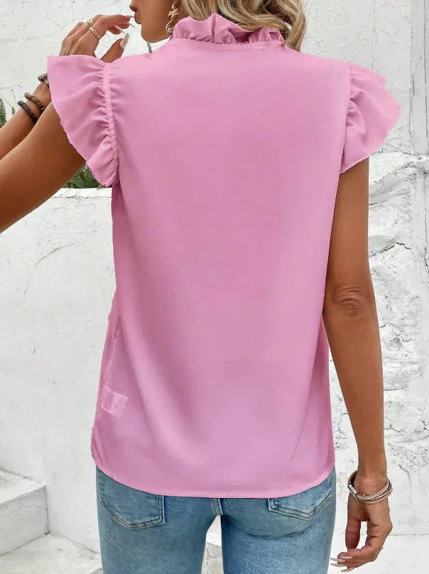 woman wearing a pink ruffle cap sleeve blouse paired with blue jeans against a white textured wall