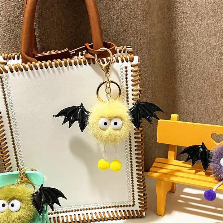 Yellow fluffy bat keychain with big eyes hanging on white leather handbag with brown handles