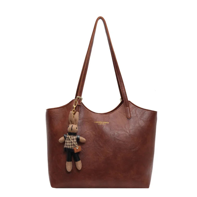 Brown leather tote handbag with long handles and a rabbit doll keychain accessory