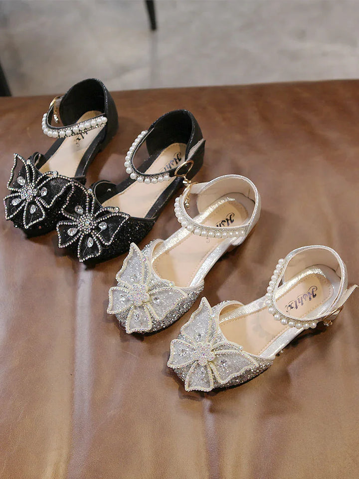 Pair of black and white glittery girls' shoes with pearl ankle straps and large decorative bows
