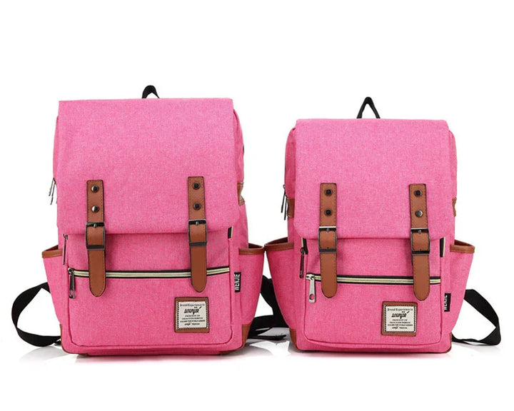 Two pink fabric backpacks with brown leather straps, front zipper pockets, and black adjustable shoulder straps